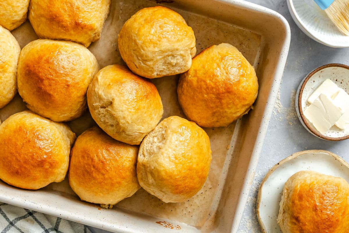 A pan with honey wheat rolls on their side next to a dish of butter. 