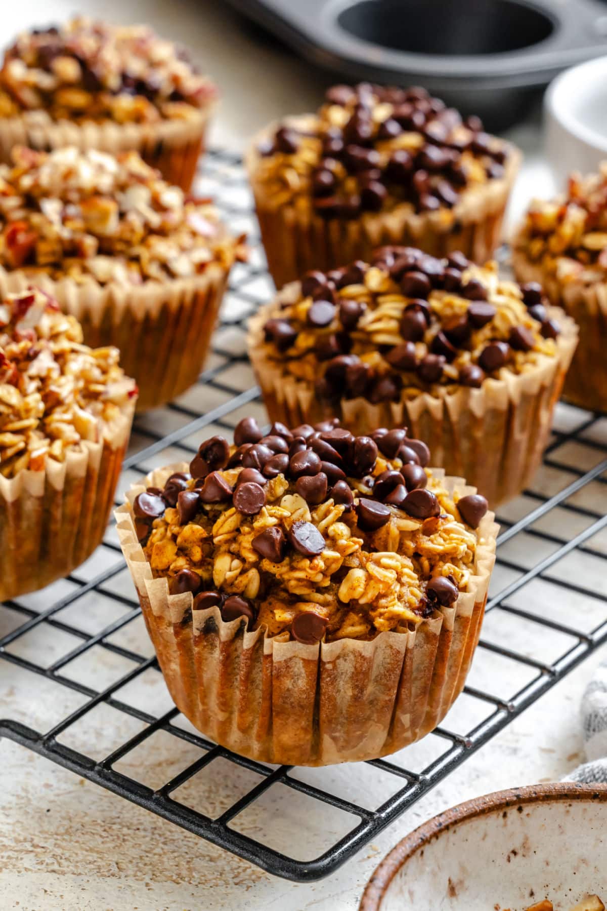 Pumpkin oatmeal cups topped with mini chocolate chips on a wire rack.