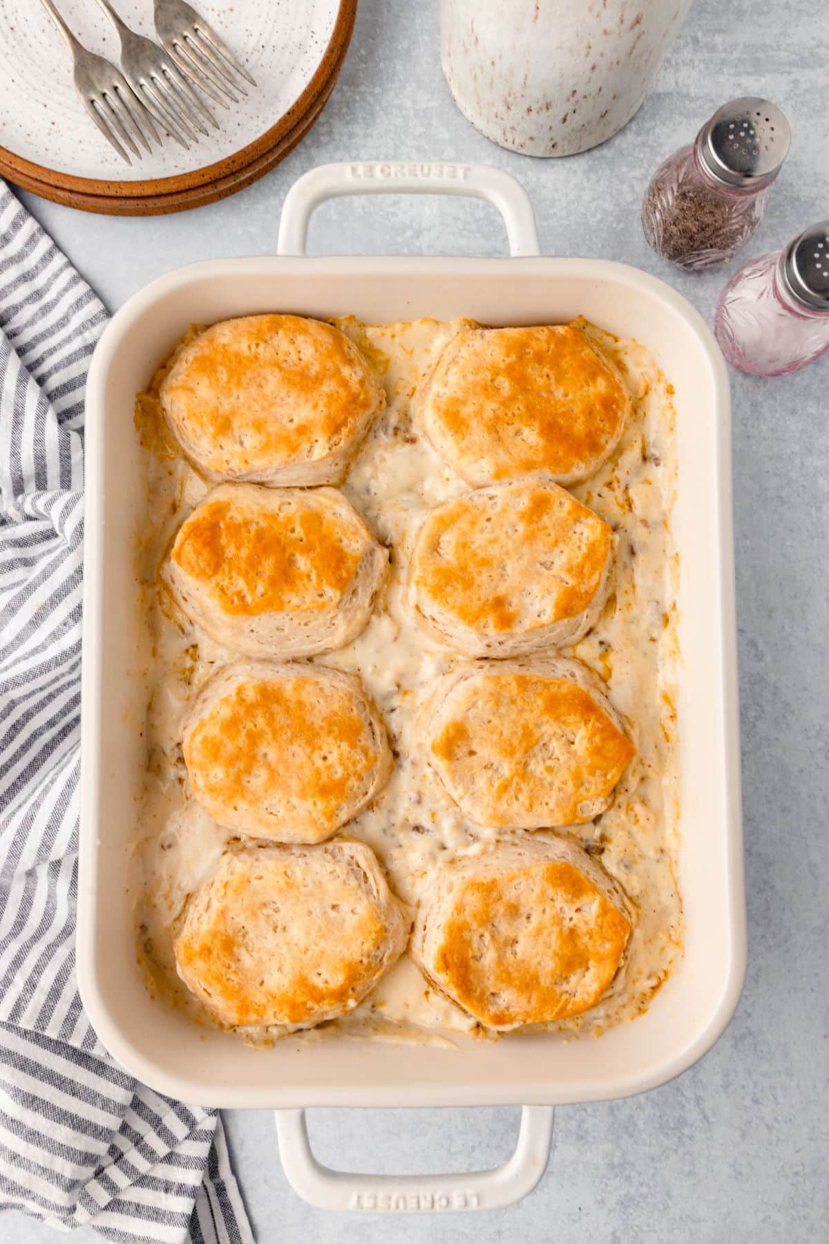 A baked biscuits and gravy casserole in a pan next to salt and pepper shakers. 