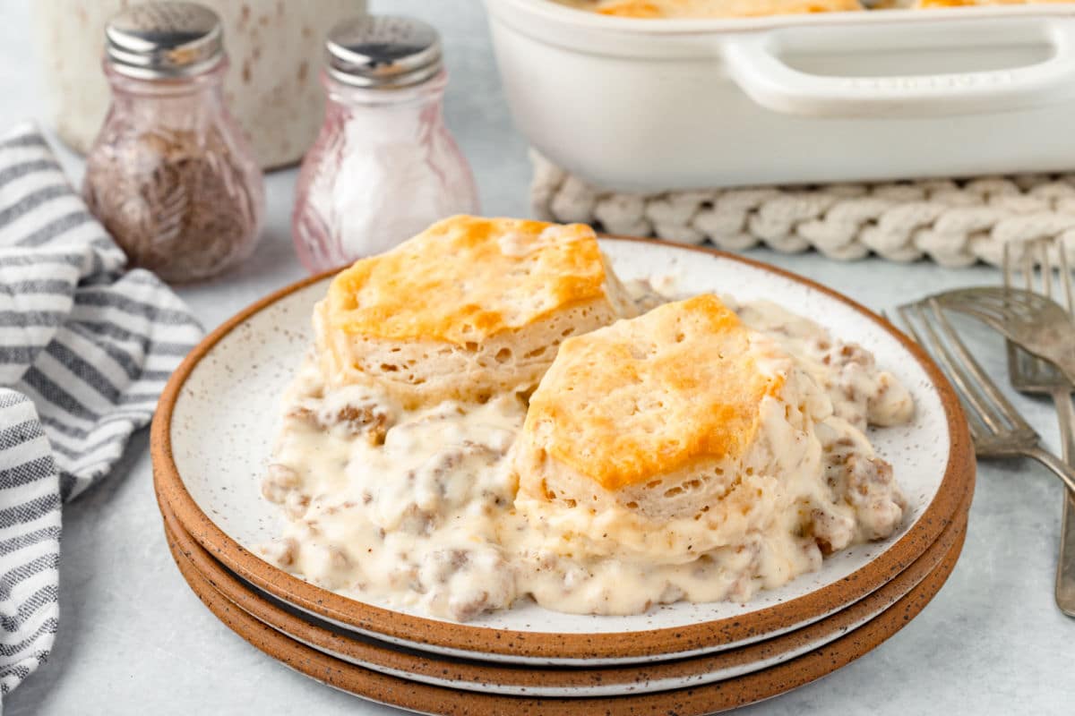 A plate with two biscuits and gravy next to the casserole dish.