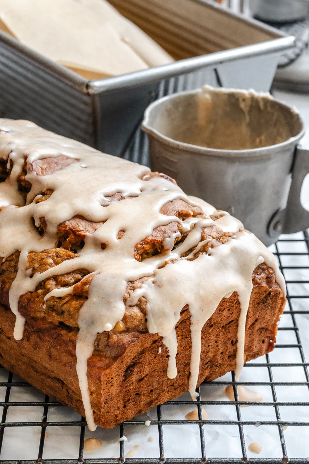 A loaf of glazed banana bread next to a cup of glaze. 