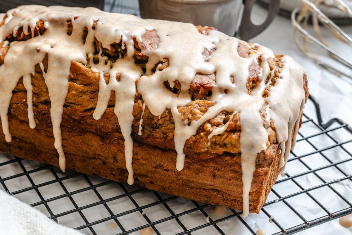 A loaf of iced banana bread on a wire cooling rack. 