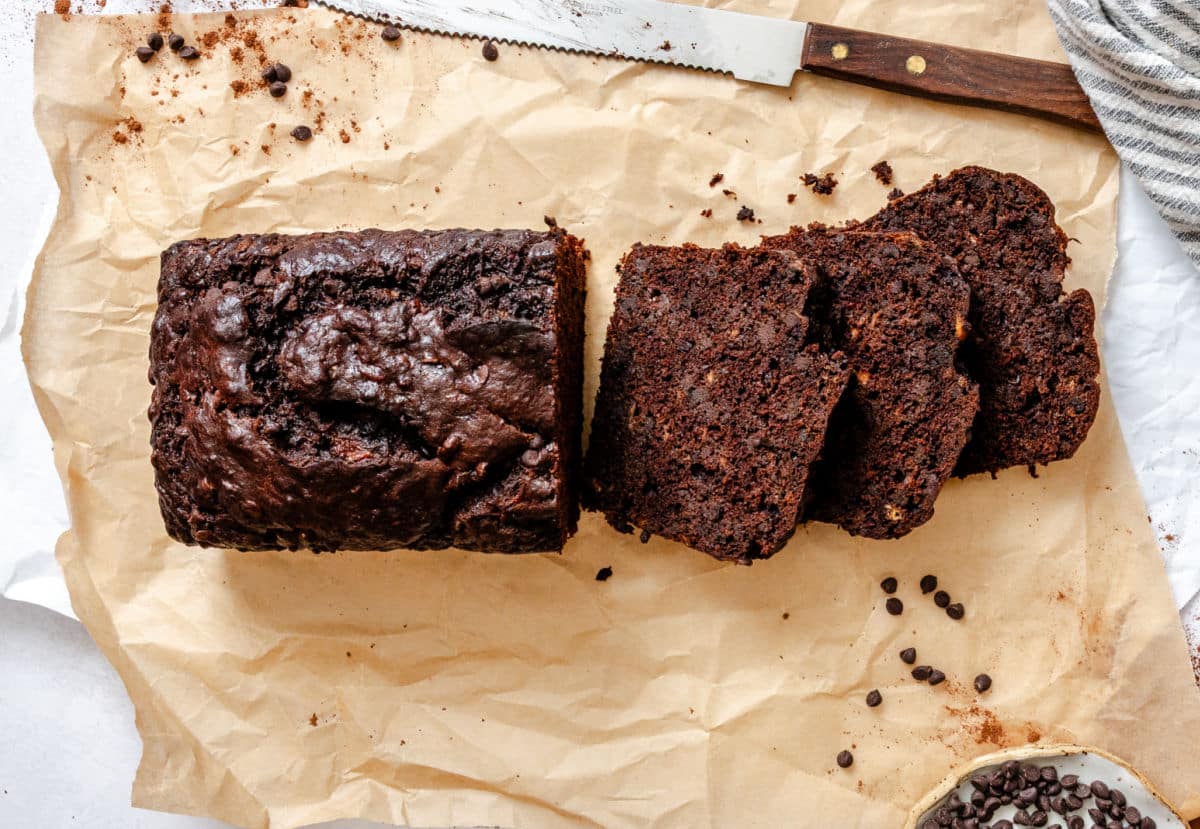 A partially sliced loaf of chocolate banana bread on brown parchment paper.