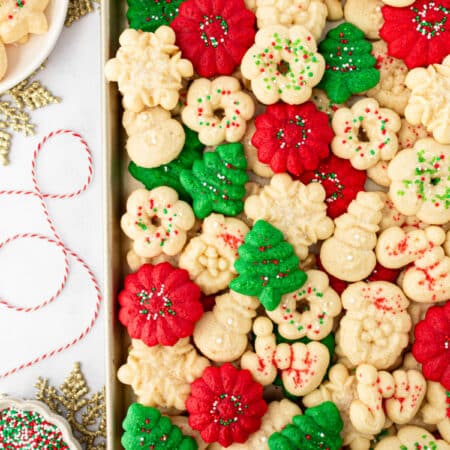 A tray of spritz cookies next to sprinkles and ribbon.