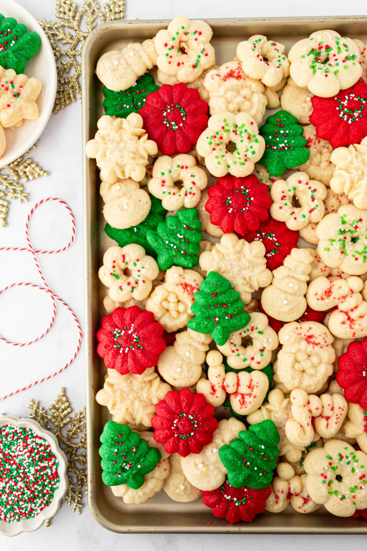 A tray of spritz cookies next to sprinkles and ribbon.