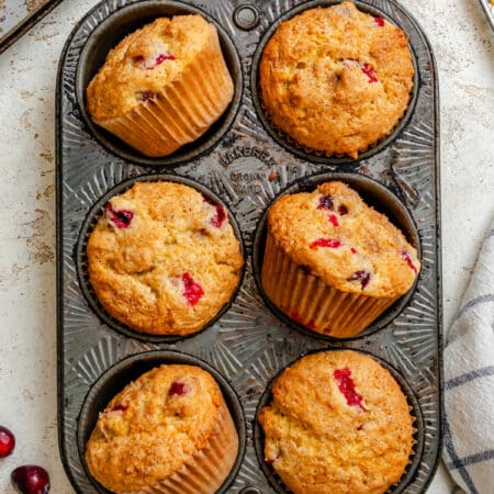 Six cranberry orange muffins at different angles in a muffin tin.
