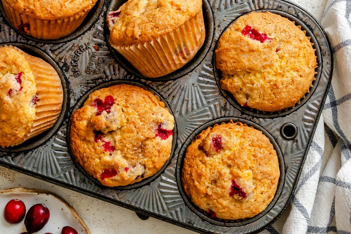Cranberry orange muffins in a muffin tin next to a dish of fresh cranberries. 
