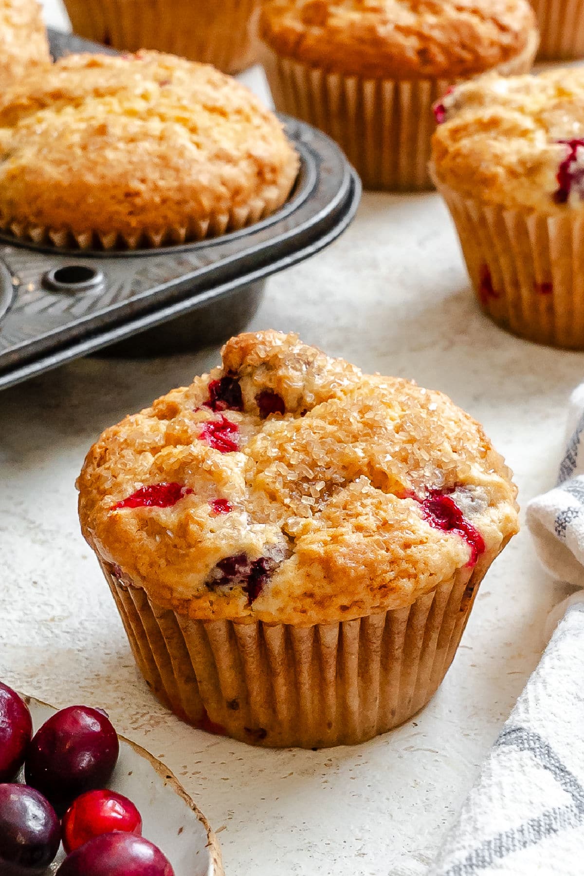 A cranberry orange muffin next to the pan of muffins. 