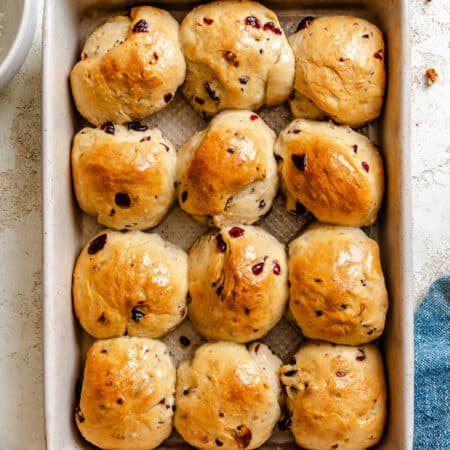 A pan of cranberry wild rice rolls next to a dish of chopped pecans and cranberries.