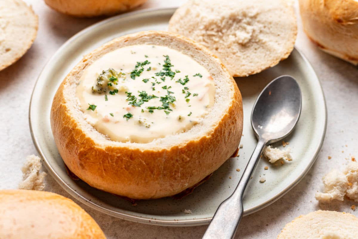 A homemade bread bowl filled with broccoli soup and topped with fresh parsley.