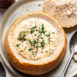 A homemade bread bowl filled with cream soup next to a spoon on a plate.
