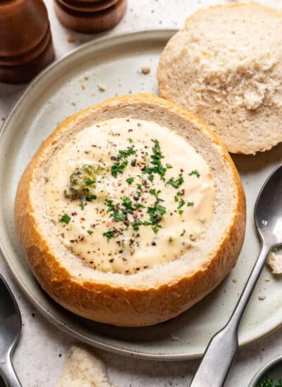 A homemade bread bowl filled with cream soup next to a spoon on a plate.