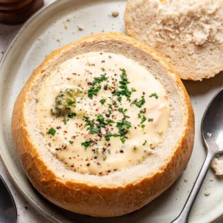 A homemade bread bowl filled with cream soup next to a spoon on a plate.