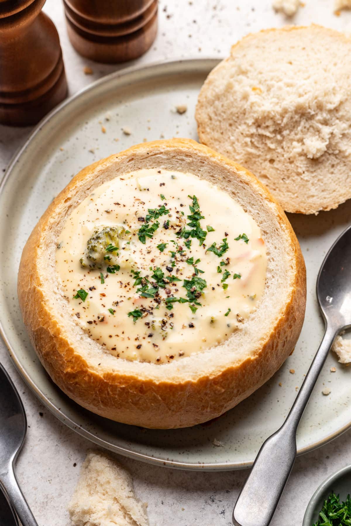 A homemade bread bowl filled with cream soup next to a spoon on a plate.