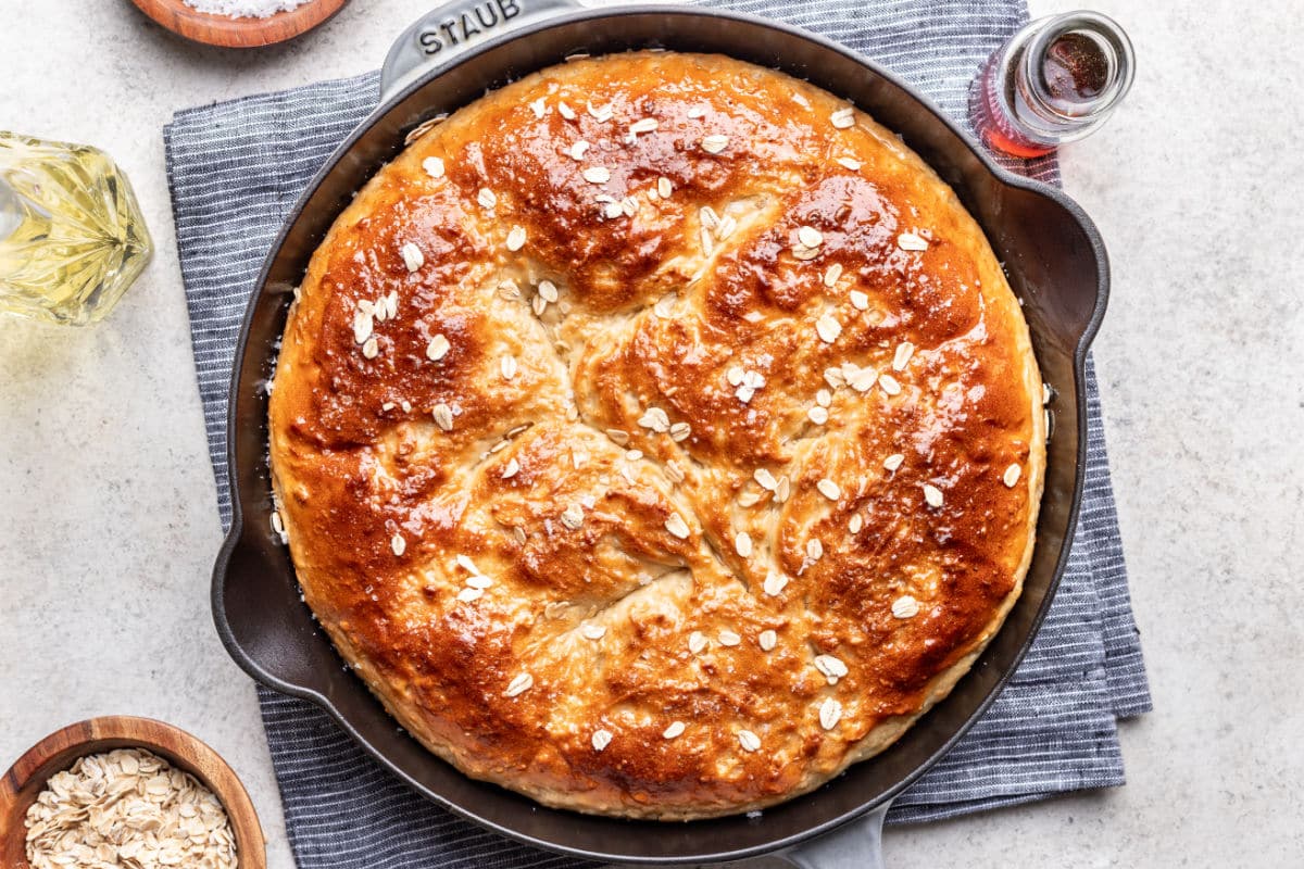 Maple oat skillet bread in a cast iron skillet next to dishes of maple syrup and oats.