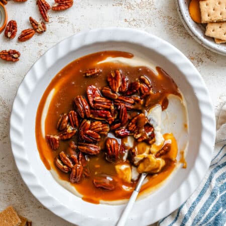 A dish of pecan pie dip with a spoon in it next to scattered pecans.