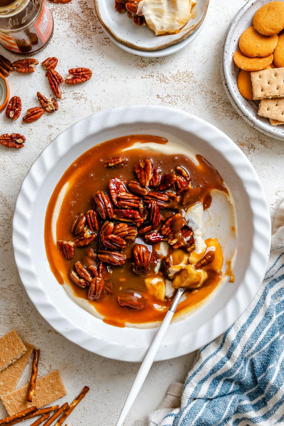 A dish of pecan pie dip with a spoon in it next to scattered pecans.