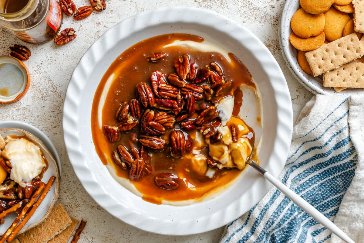 A dish of pecan pie dip next to bowls of cookies and pretzels. 