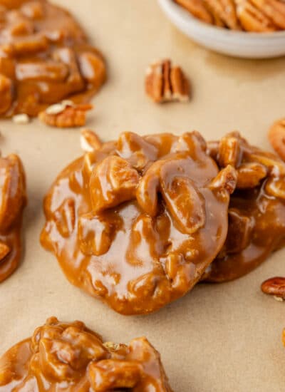 A pecan praline leaning against another praline on a piece of brown parchment paper.