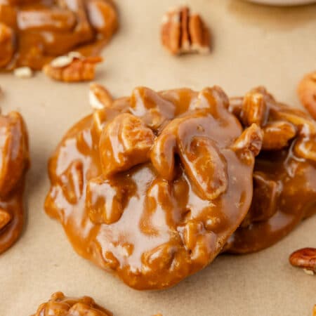 A pecan praline leaning against another praline on a piece of brown parchment paper.