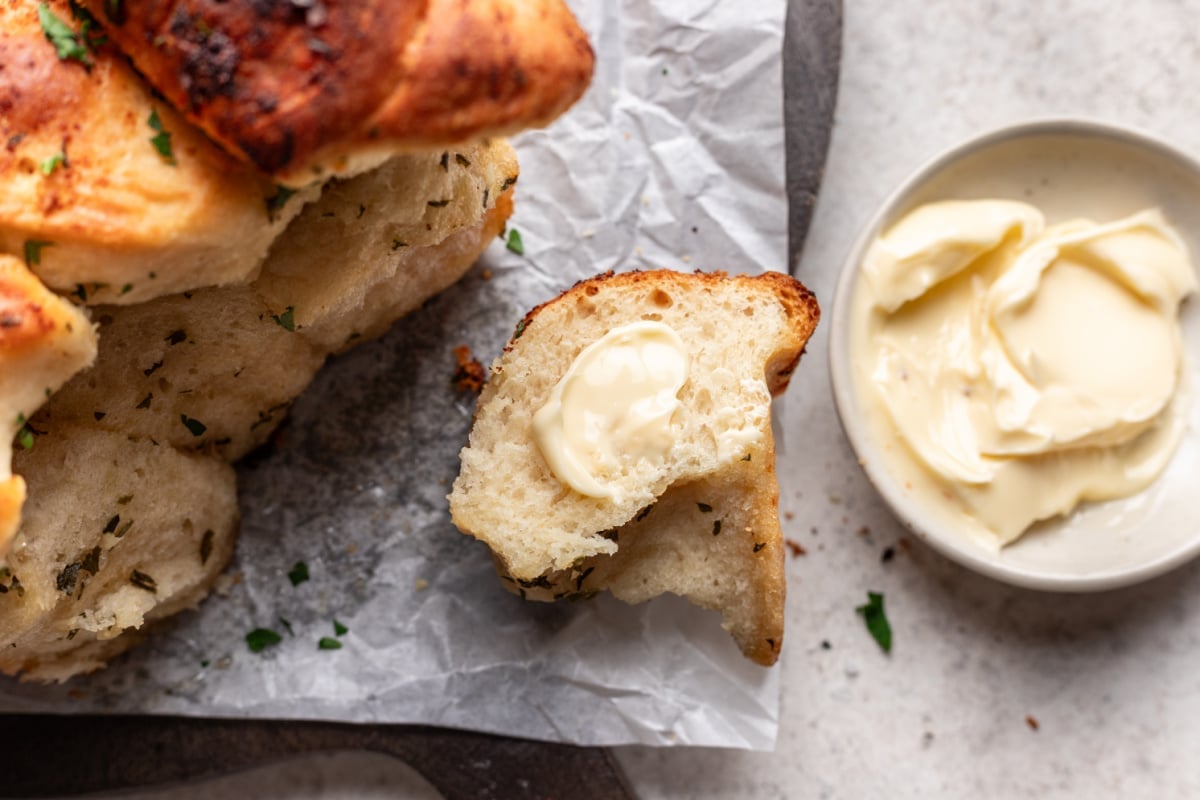 A buttered piece of garlic pull apart bread next to the loaf.