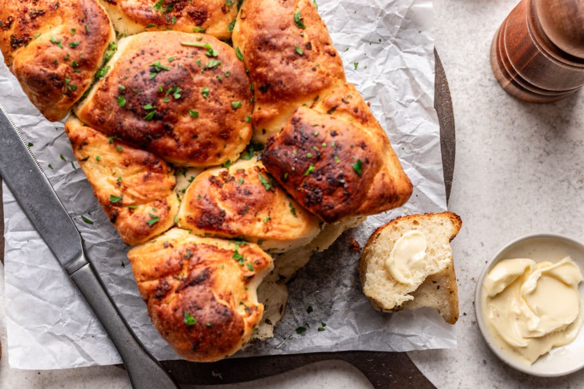 Pieces of garlic pull apart bread next to the loaf and a dish of butter.