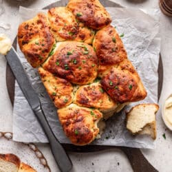 A loaf of garlic pull apart bread on a cutting board next to dishes of butter and salt.