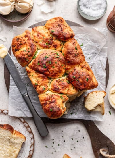A loaf of garlic pull apart bread on a cutting board next to dishes of butter and salt.