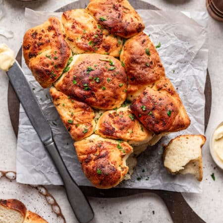 A loaf of garlic pull apart bread on a cutting board next to dishes of butter and salt.