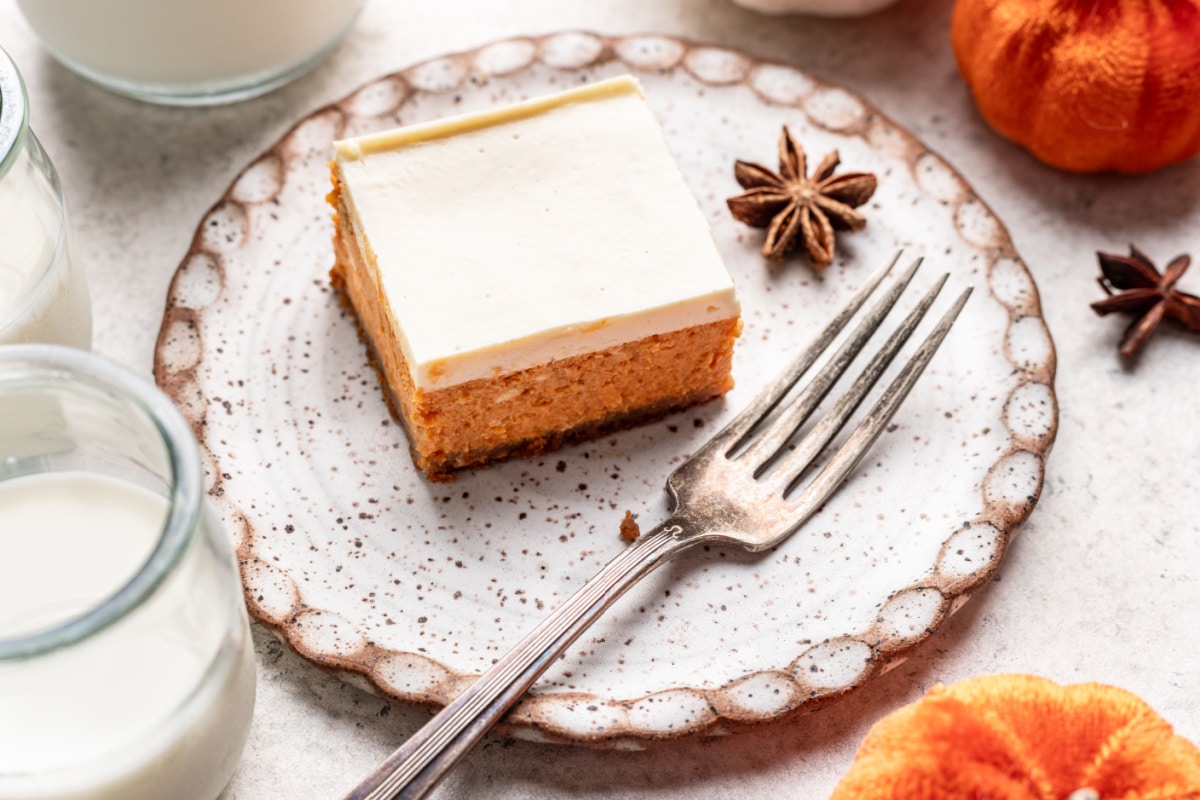 A pumpkin cheesecake bar on a plate with a silver fork.