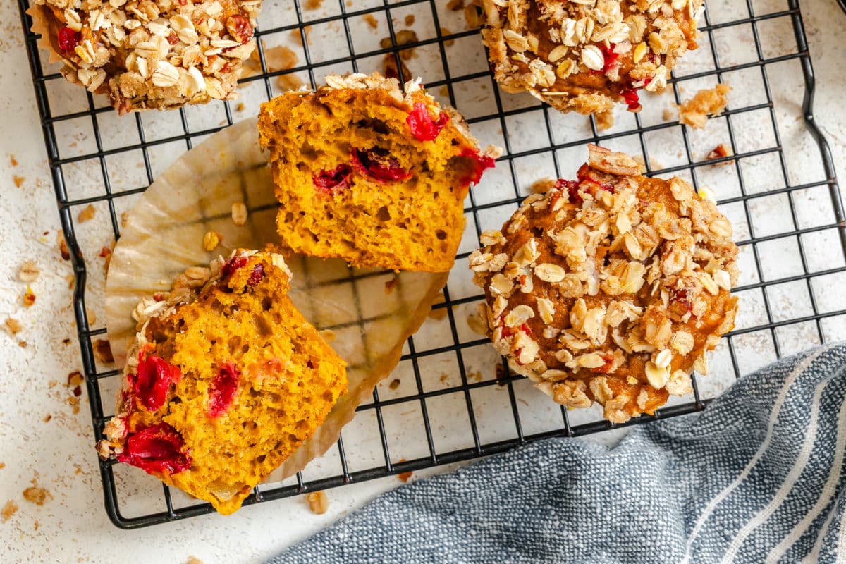 A pumpkin cranberry apple muffin cut in half on a wire cooling rack. 