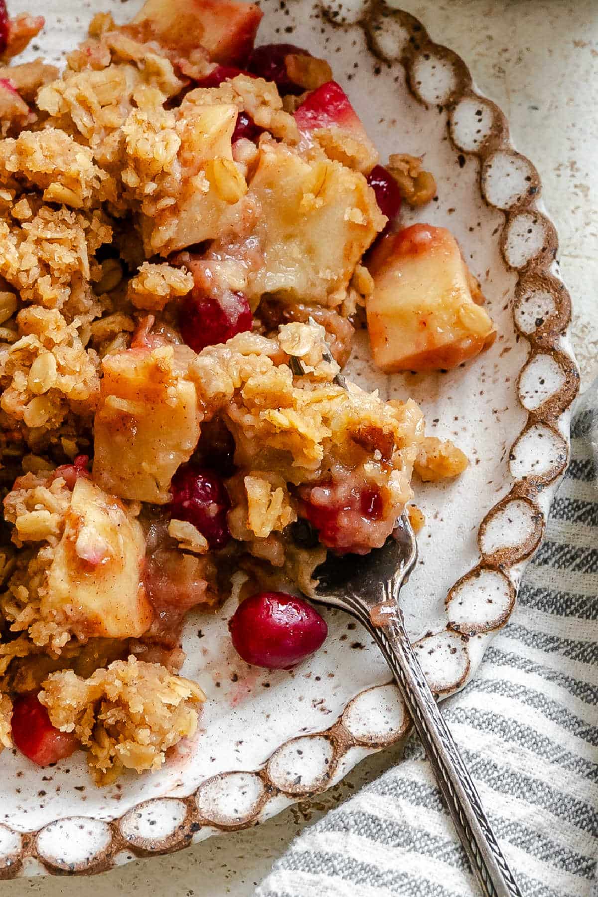 A fork taking a bite of cranberry apple crisp on a plate. 