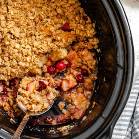 A spoon scooping up cranberry apple crisp out of a slow cooker.