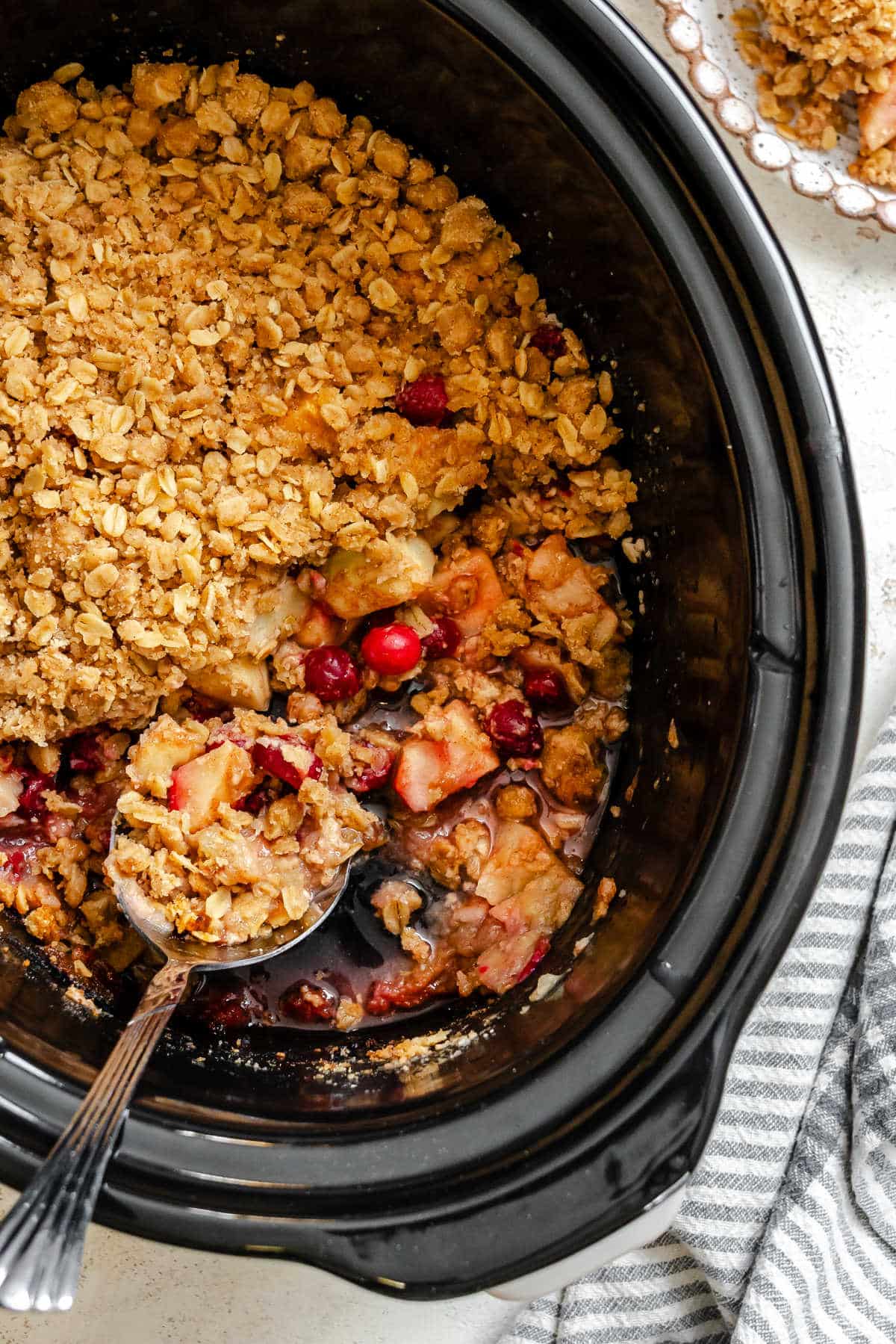 A spoon scooping up cranberry apple crisp out of a slow cooker. 