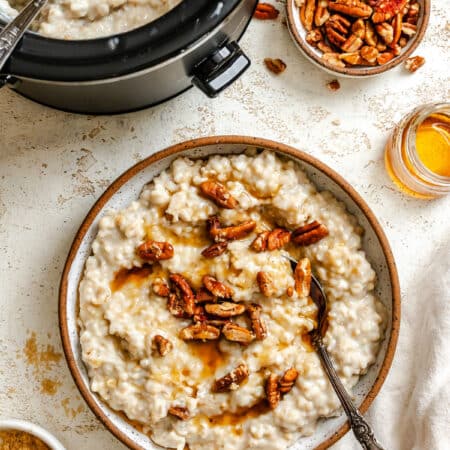 A bowl of slow cooker pecan pie oatmeal next to oatmeal in the crock pot.