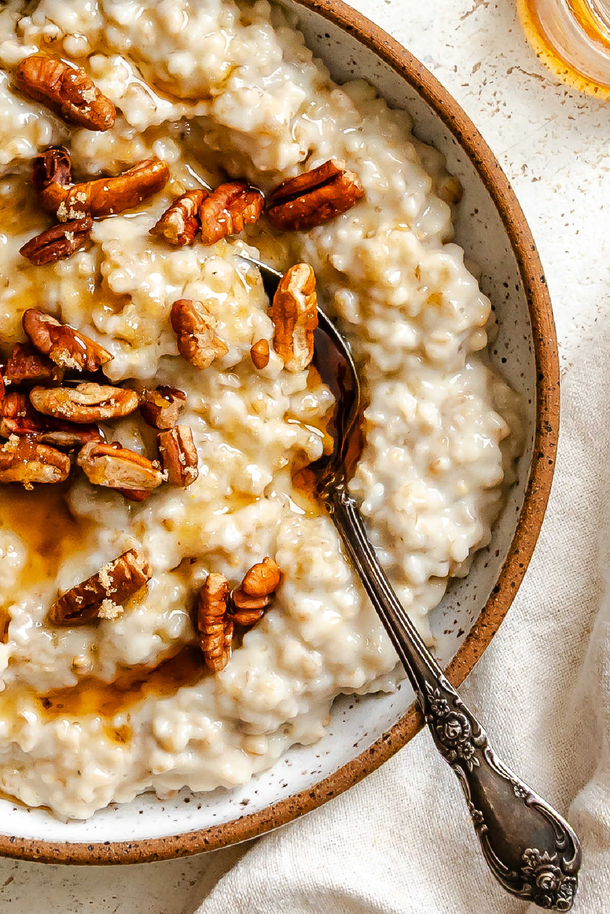 A bowl of oatmeal with a spoon in it topped with pecans and maple syrup. 