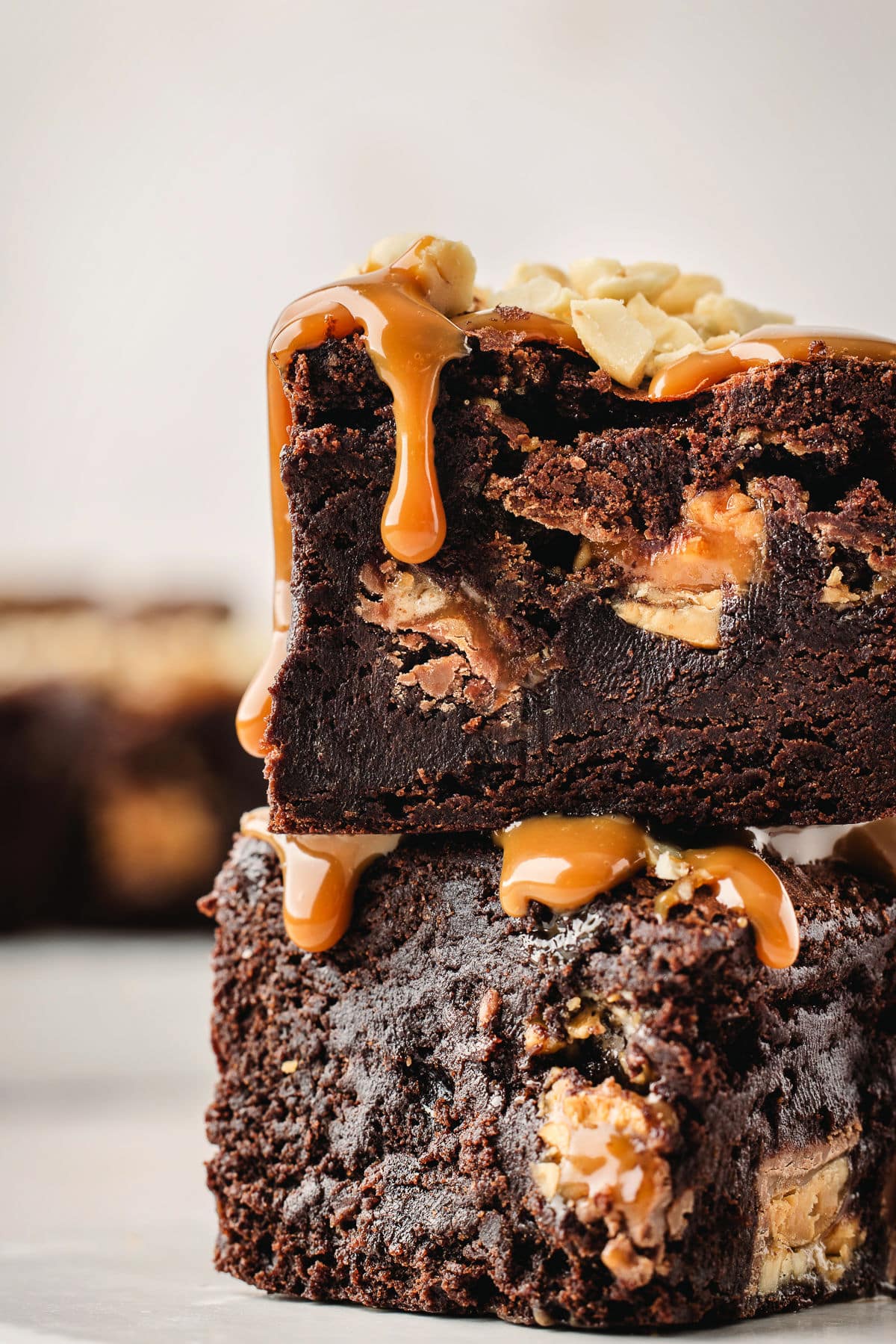 Two snickers brownies on each other with caramel dripping down the top brownie.