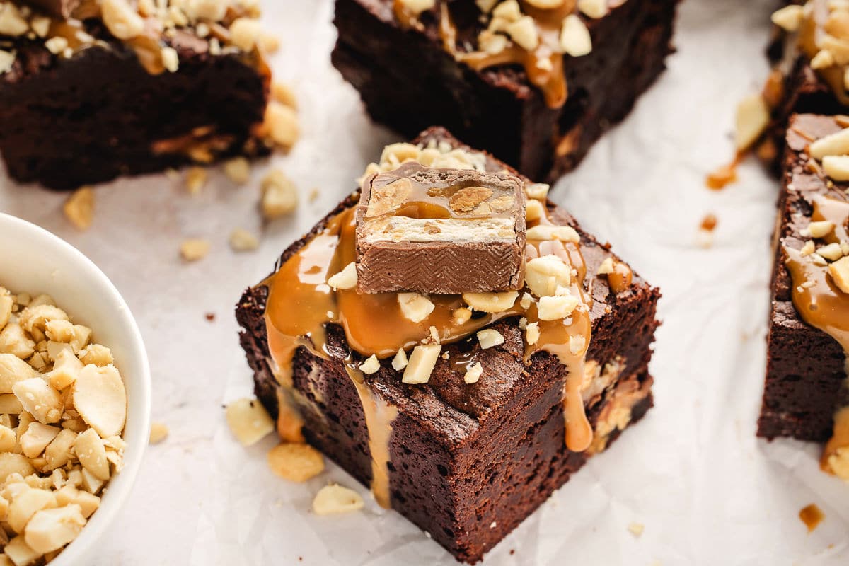 A snickers brownie next to a bowl of chopped peanuts.