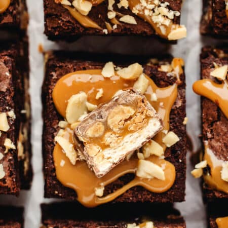 Cut snickers brownies topped with a dollop of caramel, a piece of snickers, and chopped peanuts.