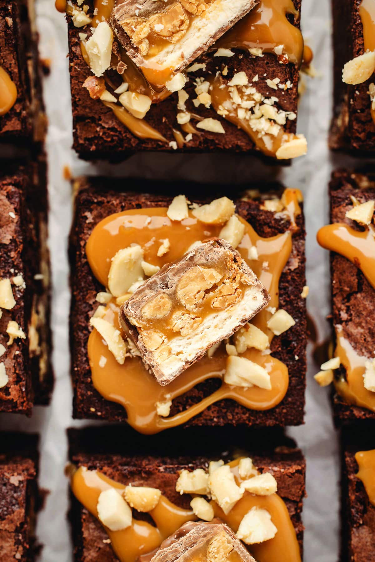 Cut snickers brownies topped with a dollop of caramel, a piece of snickers, and chopped peanuts.