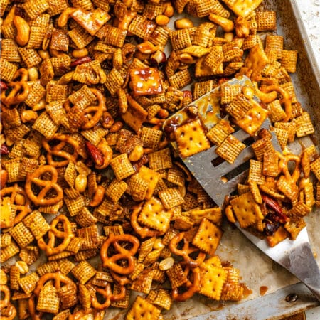 A silver spatula scooping up toffee chex mix in a baking sheet.