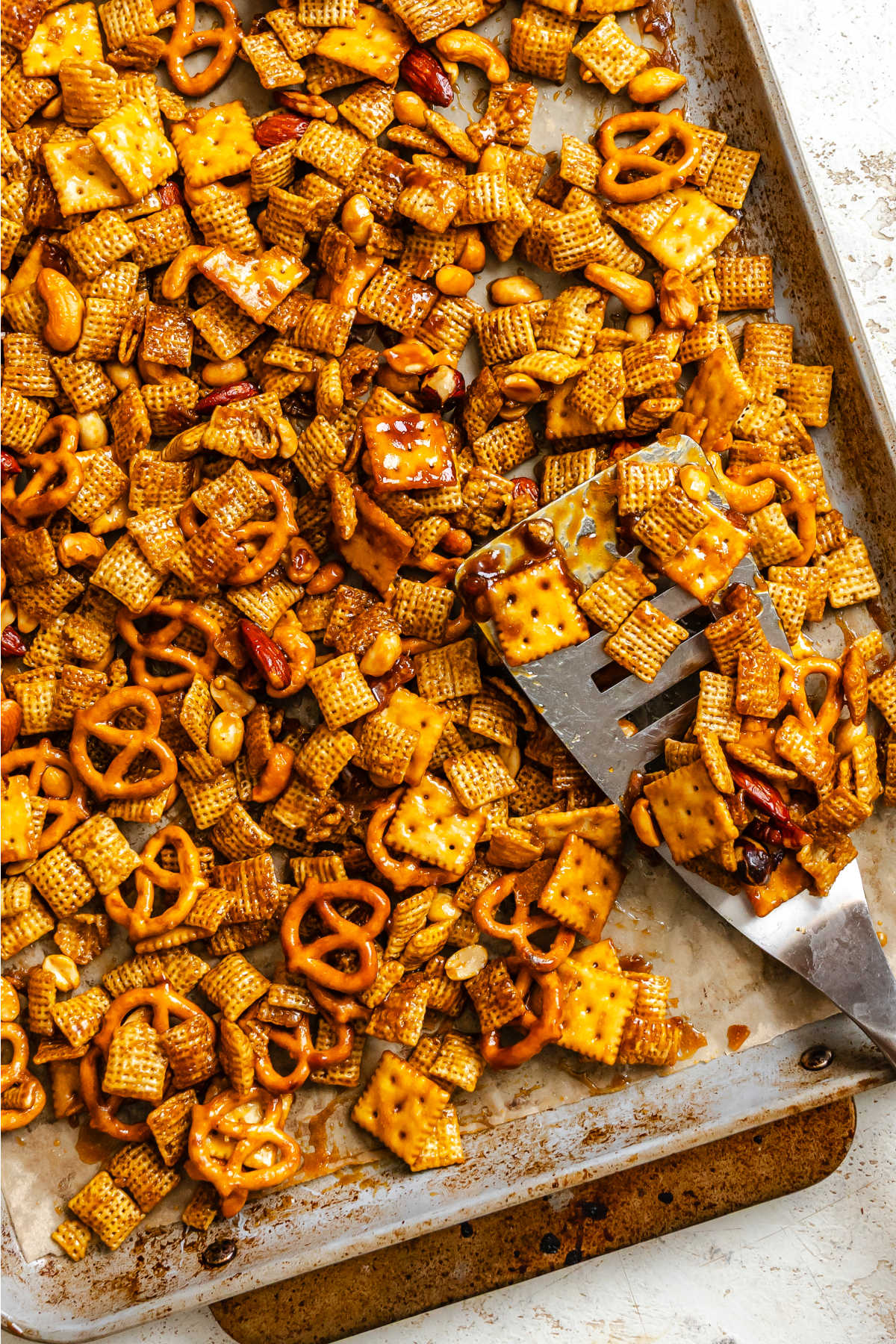 A silver spatula scooping up toffee chex mix in a baking sheet.