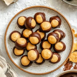 A plate of buckeyes candy next to a dish of melted chocolate.