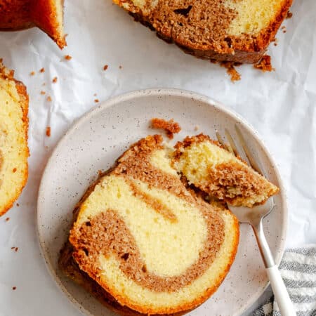 A fork taking a bite of a piece of cinnamon swirl bundt cake on a white plate.