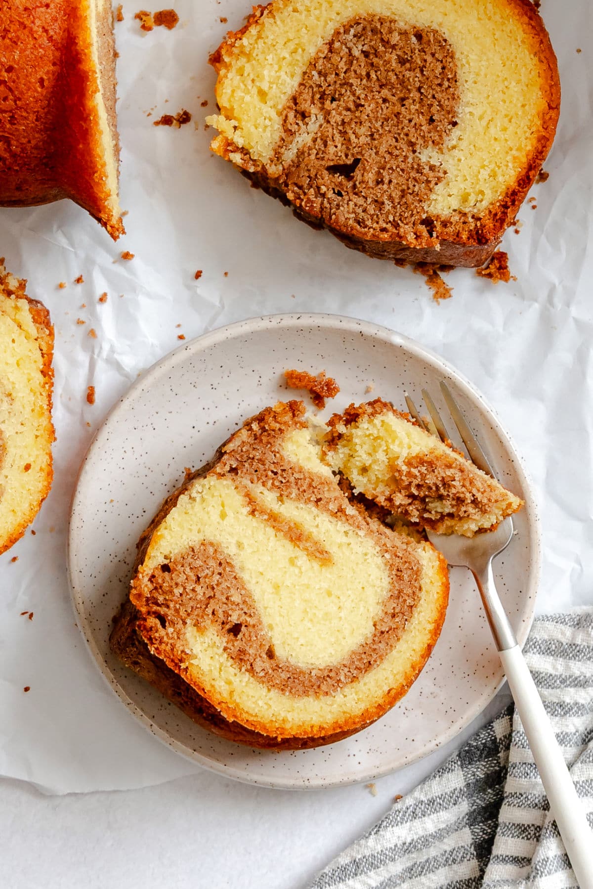 A fork taking a bite of a piece of cinnamon swirl bundt cake on a white plate.
