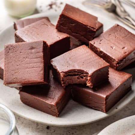 A white plate of chocolate fudge next to glasses of milk.