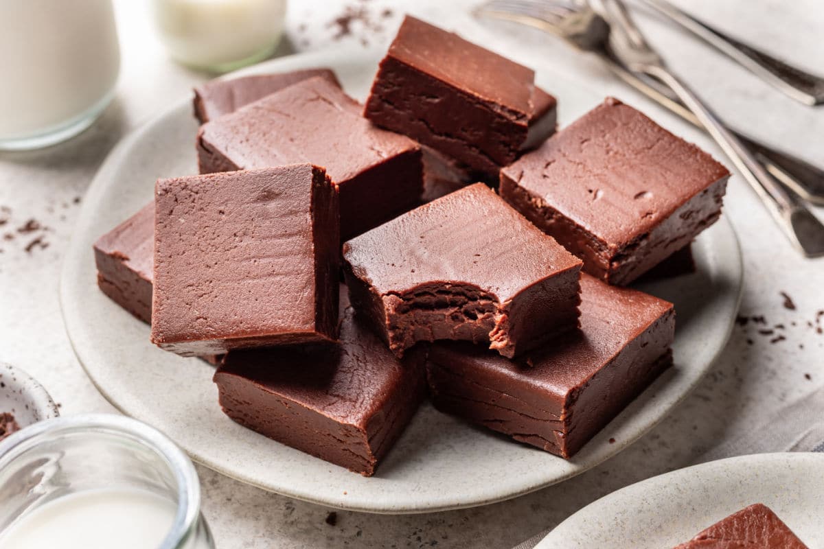 A white plate of chocolate fudge next to glasses of milk. 