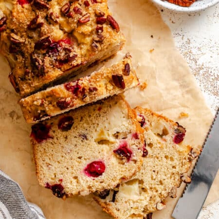 A loaf of cranberry apple bread with three slices cut.