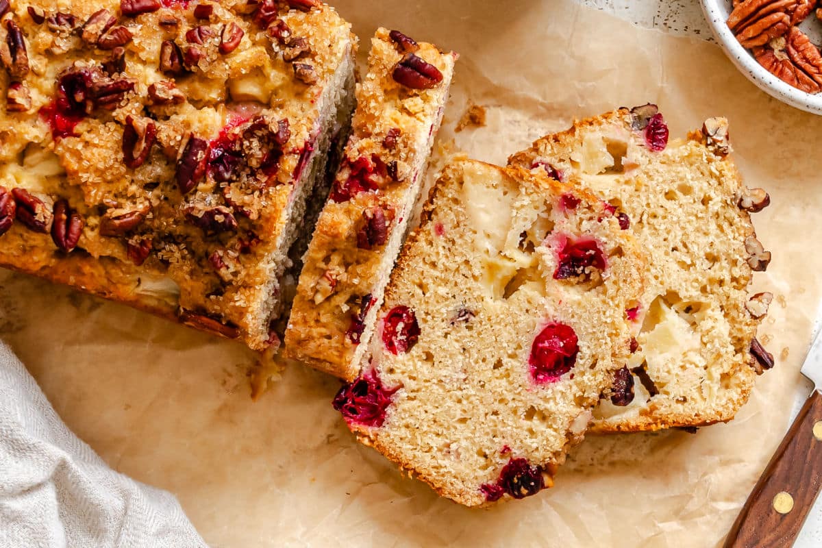 A partially sliced loaf of cranberry apple bread on brown parchment paper.