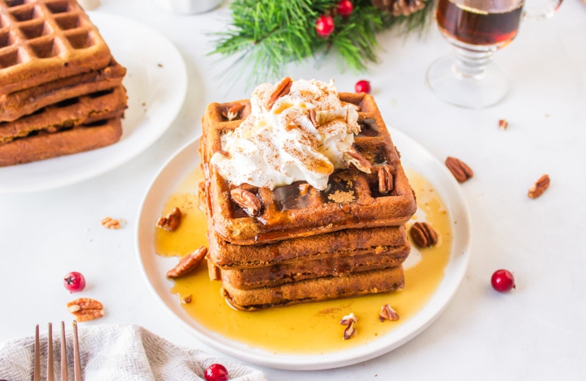 A plate of gingerbread waffles topped with whipped cream and syrup.